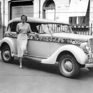 Woman standing beside vintage car, street scene.