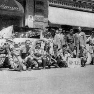 Vintage group with motorcycles and cars outside building.