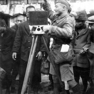 Soldier using camera surrounded by curious crowd.