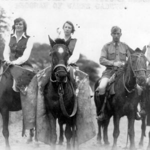 Four people riding horses in vintage attire.