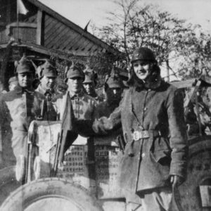 Soldiers posing with military vehicle and flags.