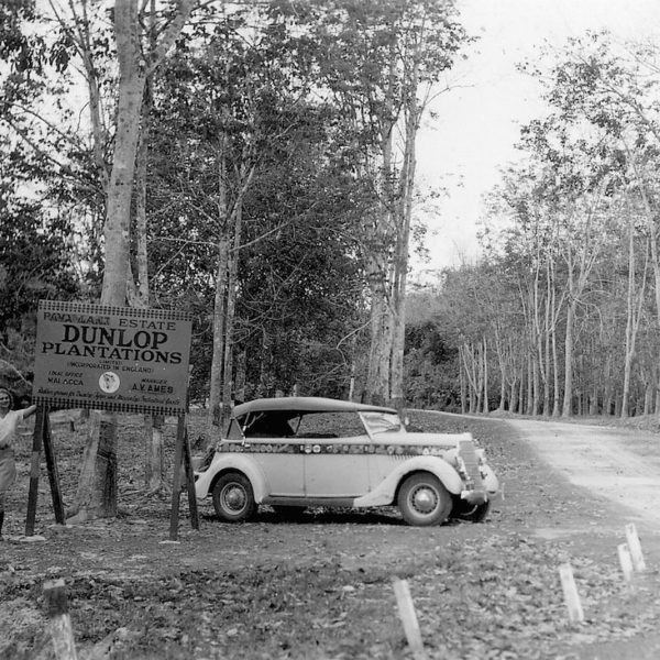 Vintage car parked by Dunlop Plantations sign.