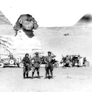 Three people posing near Sphinx and vehicles.