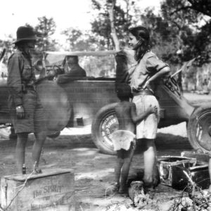 People gathered near vintage car, outdoors scene.